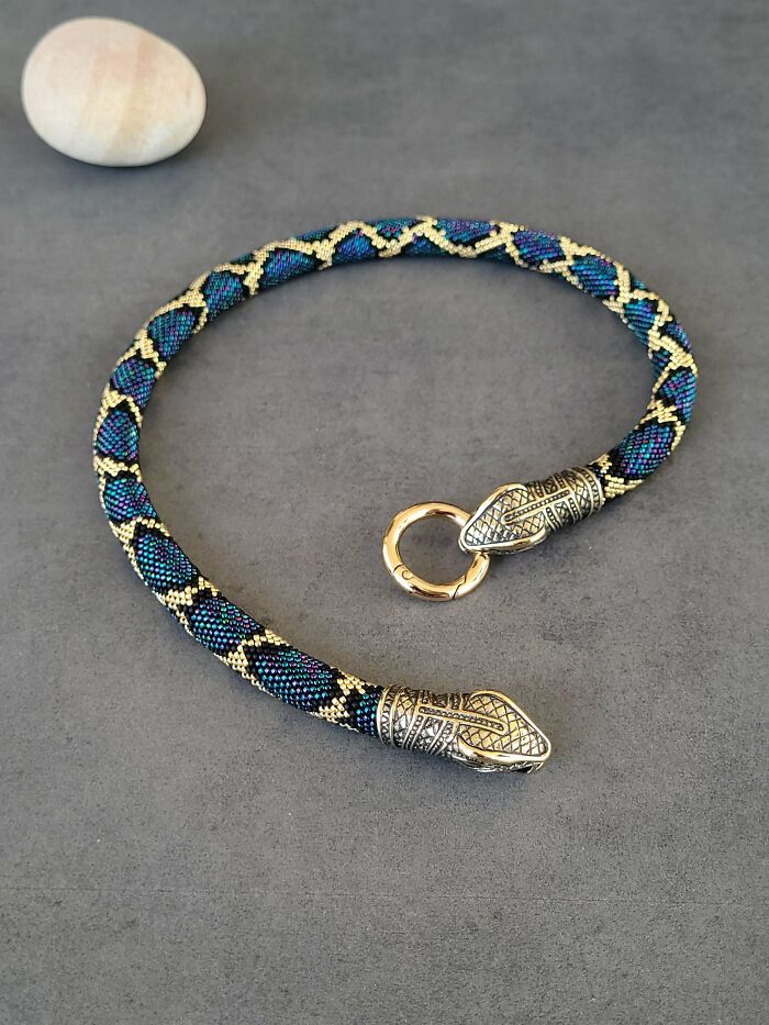 Amazing Photos beaded snake necklace with blue teal gold beads and ornate metal snake-head clasps on gray surface