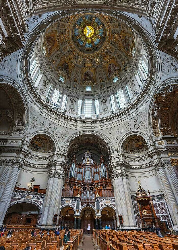 Intricate architectural feats inside a historic cathedral featuring a grand dome, detailed carvings, and wooden pews.