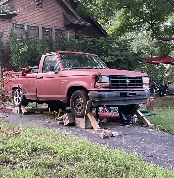 Old red pickup truck elevated with wooden blocks and jacks in yard as a redneck engineer creation.