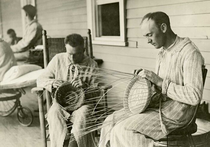 Two men weaving baskets on a porch, showcasing daily life beyond the WWI trenches in a relaxed setting.