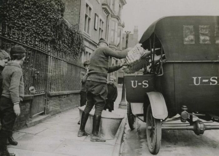 Man unloading supplies from a U.S. military vehicle with children watching, showing daily life beyond WWI trenches.