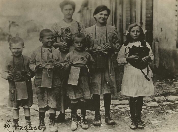 Children and women holding gas masks, revealing daily life beyond the WWI trenches in a historic black and white photo.