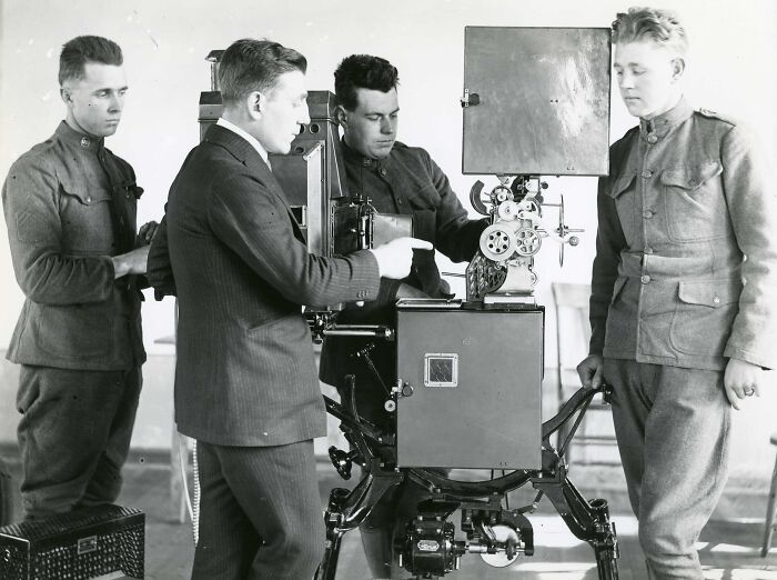 Four men, three in military uniforms, operating and inspecting early film equipment behind the WWI trenches.
