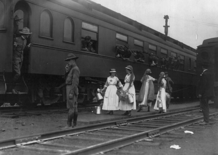 Nurses and soldiers beside a train, showing daily life beyond the WWI trenches at a railway station.