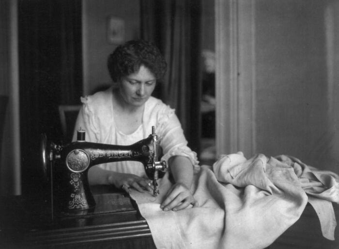 Woman using a vintage sewing machine, illustrating daily life beyond the WWI trenches with fabric and focused concentration.