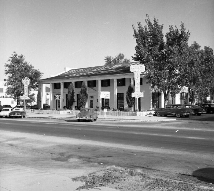 Vintage black and white photo of early Vegas street scene with classic cars parked outside historic buildings.