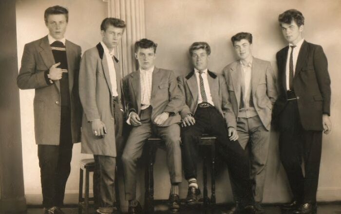 Group of six young men dressed in iconic 20th century Teddy Boy era fashion posing indoors in a vintage black and white photo.