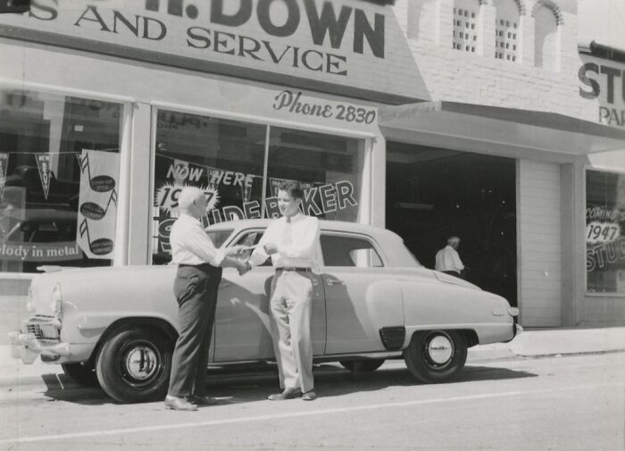 Two men shaking hands beside a vintage car in front of a 1947 storefront, capturing the birth of Vegas era.