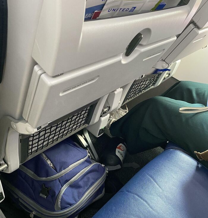 Passenger blocking airplane aisle with a large backpack placed under the seat, showing disregard for travel etiquette.