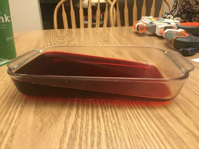 Glass dish filled with red liquid tilted on wooden table showing a funny way people learned their lesson.