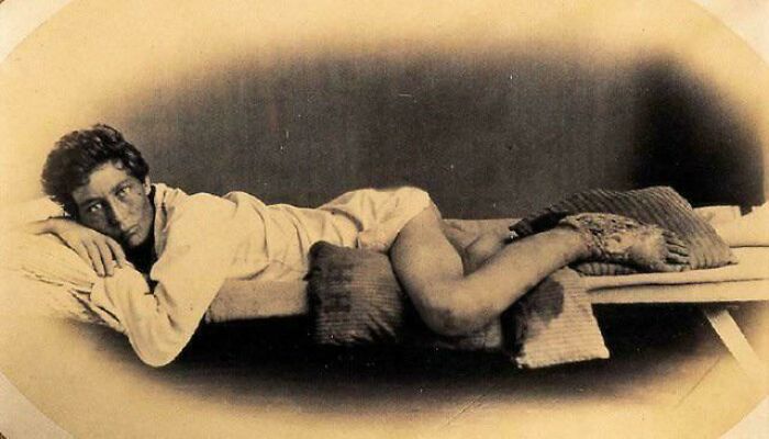 Young man lying on a simple bed, captured in a candid glimpse into the past, showing authentic historical life moments.