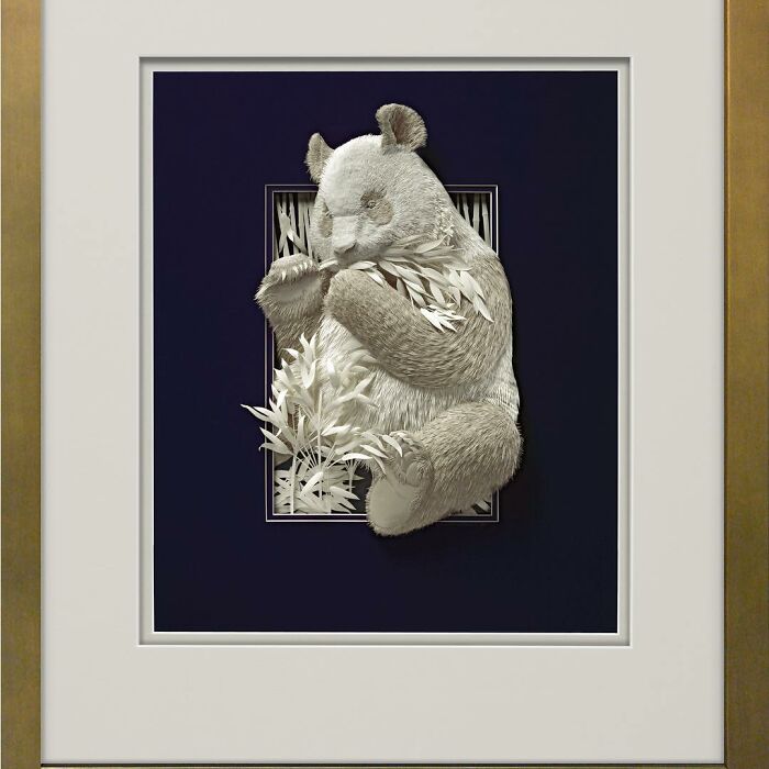Realistic wildlife sculpture of a panda eating bamboo, intricately crafted from simple paper by an artist.