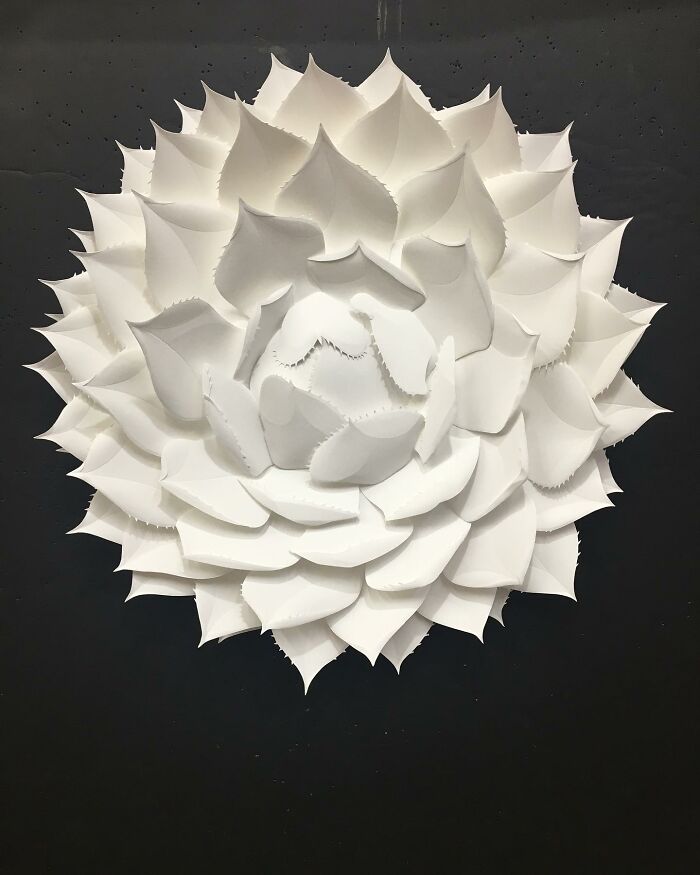 White paper sculpture resembling a layered flower, showcasing the artist's skill in creating realistic wildlife sculptures from simple paper.