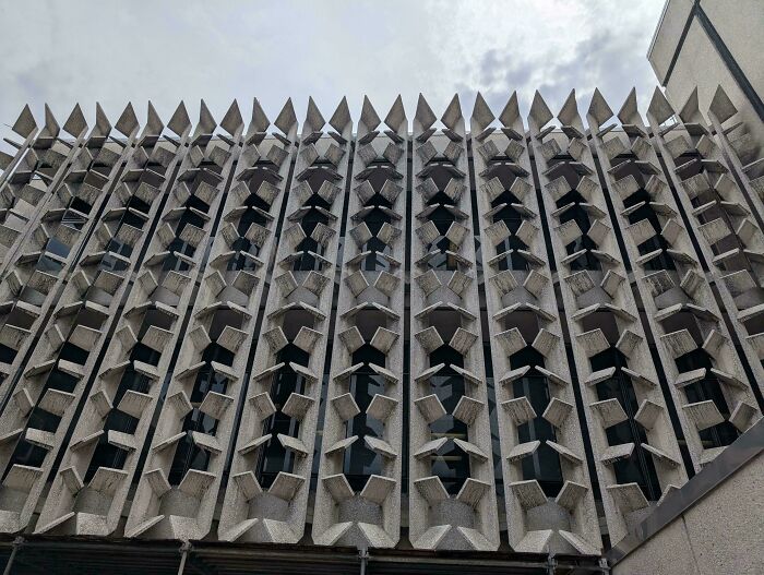 Facade of an eerie, evil building with sharp, angular concrete designs resembling horror movie architecture.