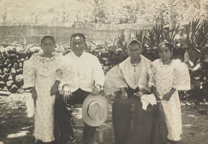 Family portrait from the Philippines in the 1890s, showing traditional clothing and rural garden setting with stone fence background.