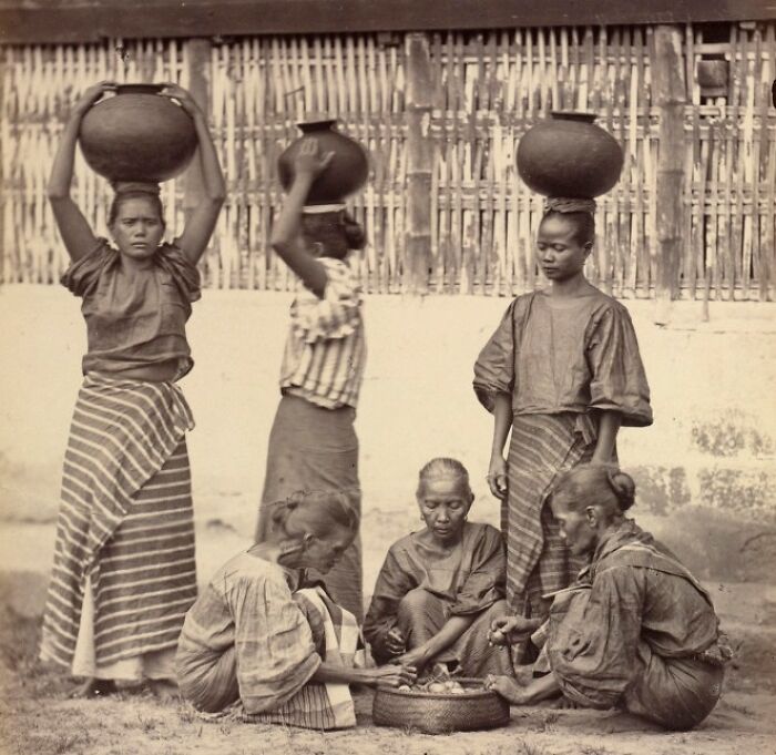 Filipino women in traditional clothing carrying pots and preparing food outdoors in the Philippines in the 1890s.