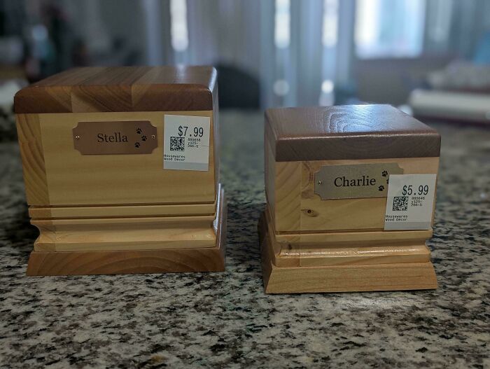 Two personalized wooden urns with nameplates labeled Stella and Charlie, priced as thrift store finds on a countertop.