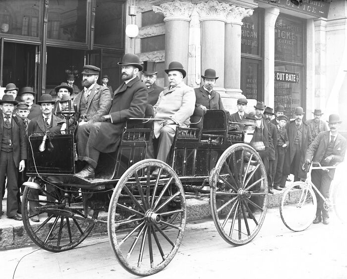 Early car with wooden spoked wheels and men in period clothing showcasing how wild the first cars really were.