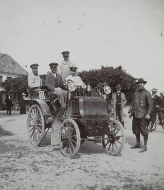 Early vintage car with passengers and bystanders, showcasing how wild the first cars really were 100 years ago.