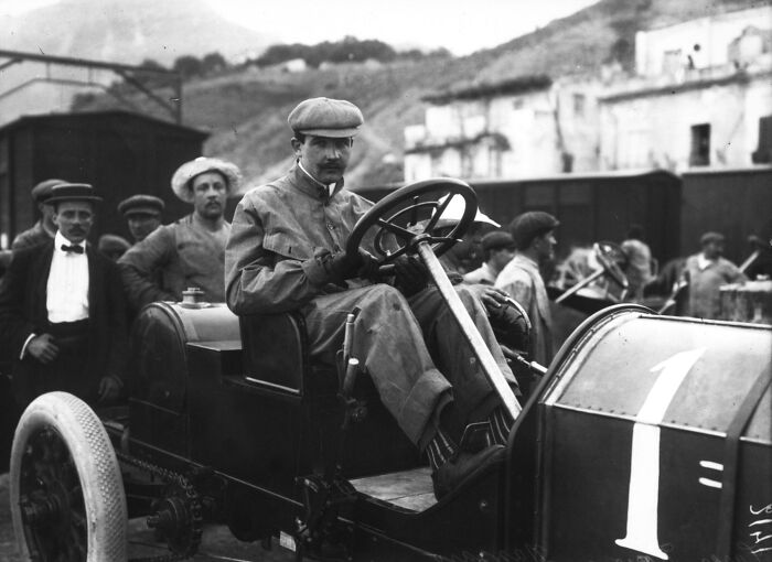 Early 20th century man driving one of the first cars, showcasing how wild the first cars really were 100 years ago.