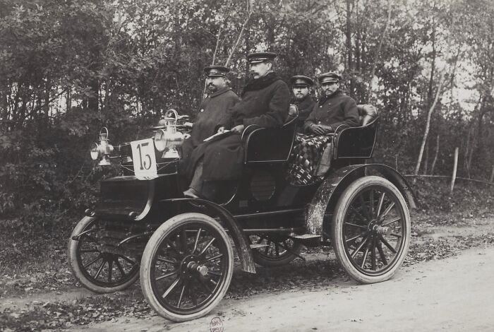Four men wearing coats and hats riding in a vintage early 1900s car, showing how wild the first cars really were.