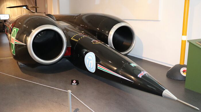 Streamlined black record-breaking invention with large jet engines displayed indoors, showcasing mind-blowing speed technology.
