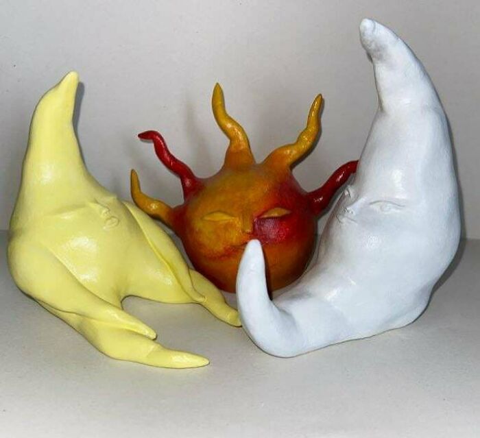 Sculptures of a yellow crescent moon, white crescent moon, and an orange sun with faces in a creative handmade art display.