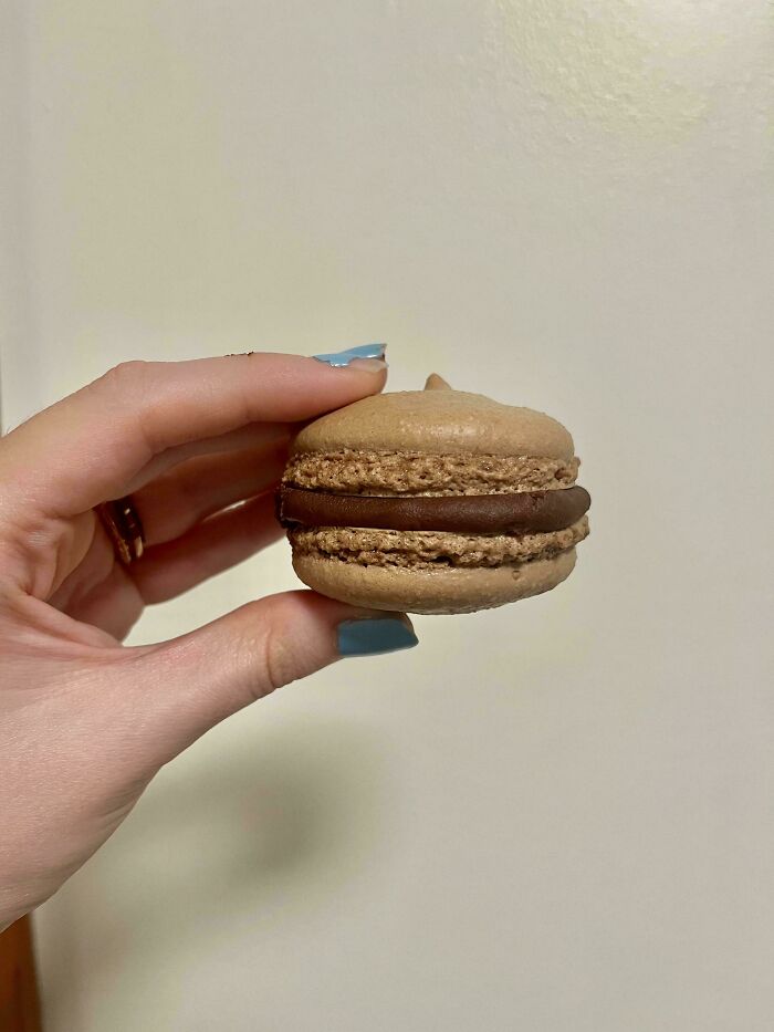 Hand holding a chocolate macaron showcasing one of the gorgeous baked goods made by kitchen magicians.