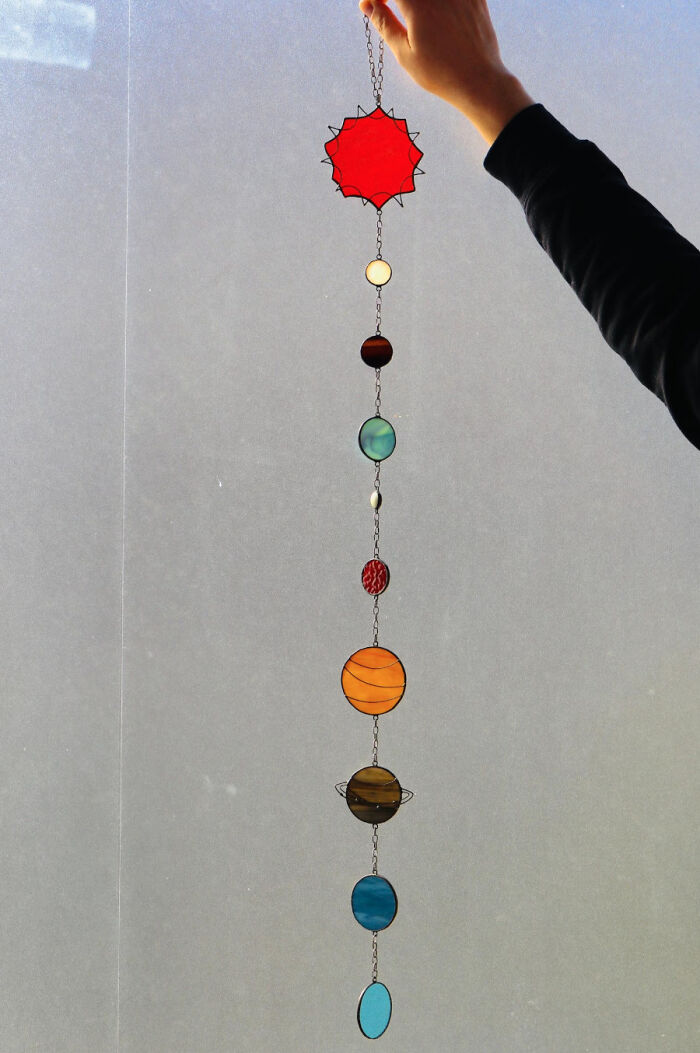 Hand holding a cool handmade stained glass solar system decoration with colorful planets on a chain.