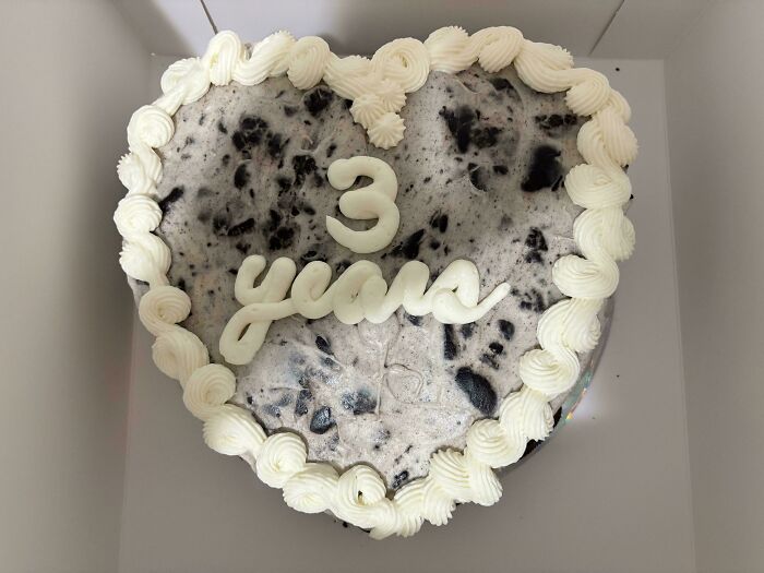 Heart-shaped cookies and cream cake with white frosting border and 3 years written on top, showcasing baked goods artistry.