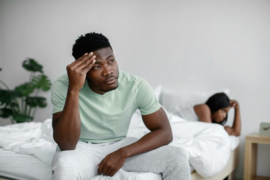 Man sitting on bed looking pensive and worried with woman lying in bed behind him, suggesting soul ties emotional struggle. Man sitting on bed looking pensive and worried with woman lying in bed behind him, suggesting soul ties emotional struggle.
