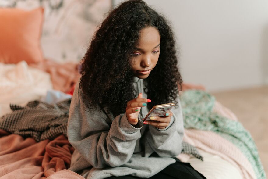 Young woman sitting on bed, looking thoughtful while using smartphone, illustrating soul ties and emotional connection concept. Young woman sitting on bed, looking thoughtful while using smartphone, illustrating soul ties and emotional connection concept.