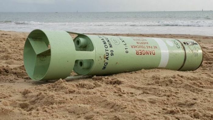 Large green military mine partially buried in sand, an interesting and bizarre thing found at the beach near the water.