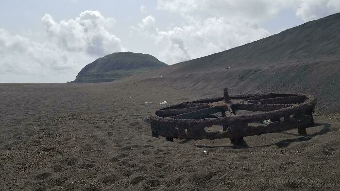 Rusty metal wheel partially buried in sand on a deserted beach, one of the interesting things people found at the beach.