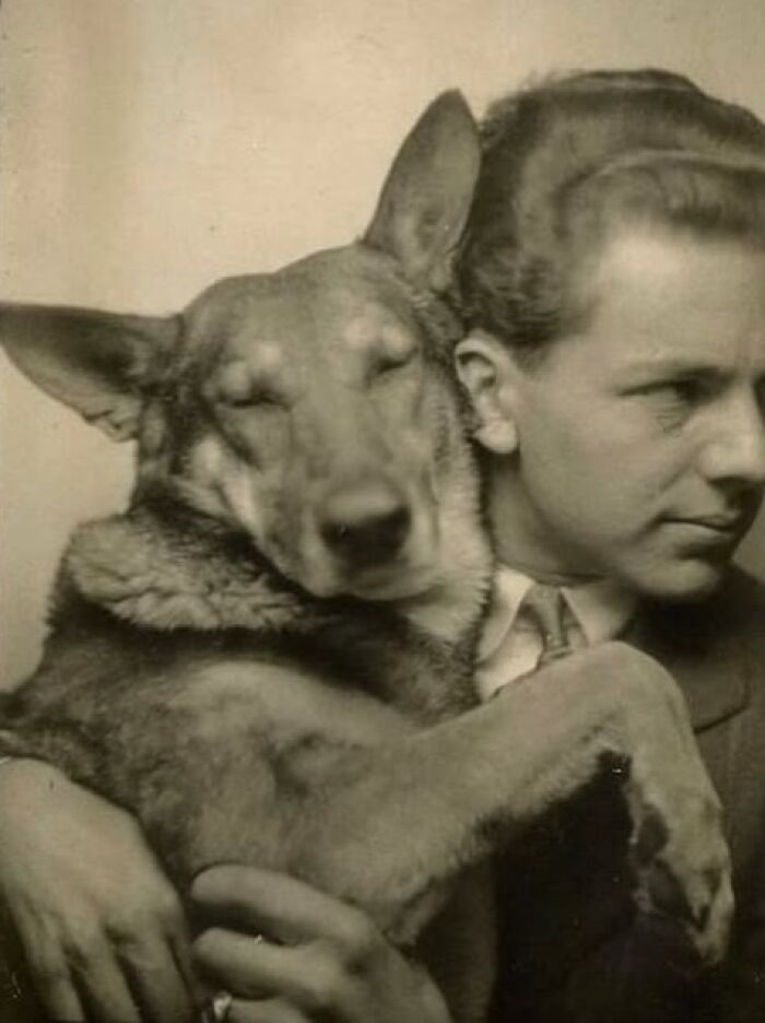 Vintage black and white photo of a man holding a relaxed dog, showcasing a historical perspective on pets and their bond.