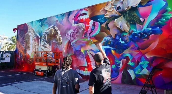 Two artists observing a vibrant graffiti mural blending realism and abstraction in an outdoor urban setting.