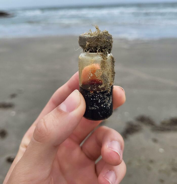 Hand holding a small old glass vial covered in sand, one of the interesting and bizarre things found at the beach.