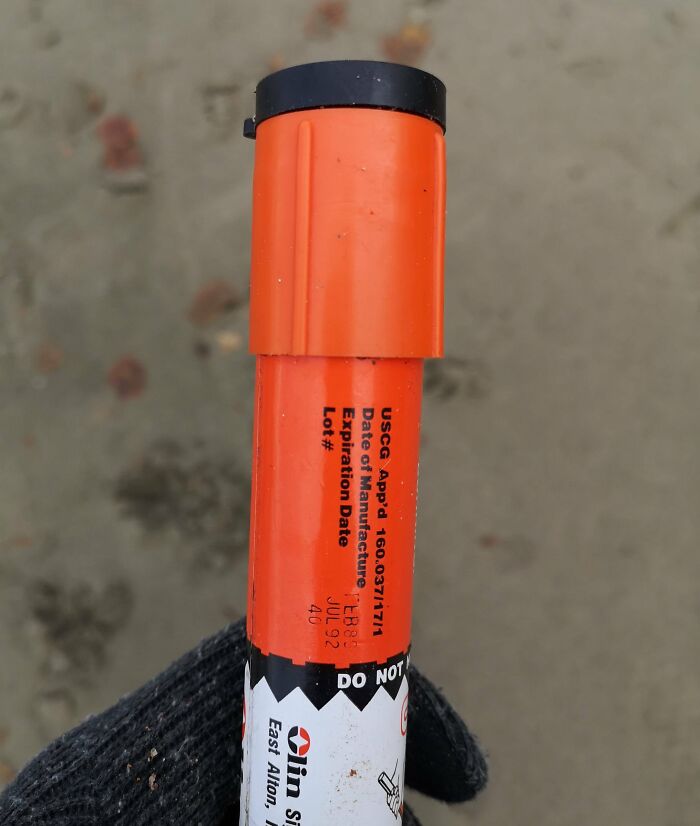 Orange safety flare with black cap found at the beach, held by a gloved hand on sandy ground.