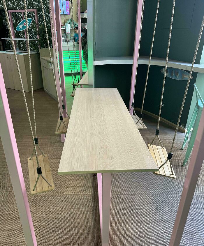 Creative bar seating with swings instead of chairs surrounding a modern wooden table in a unique restaurant interior.