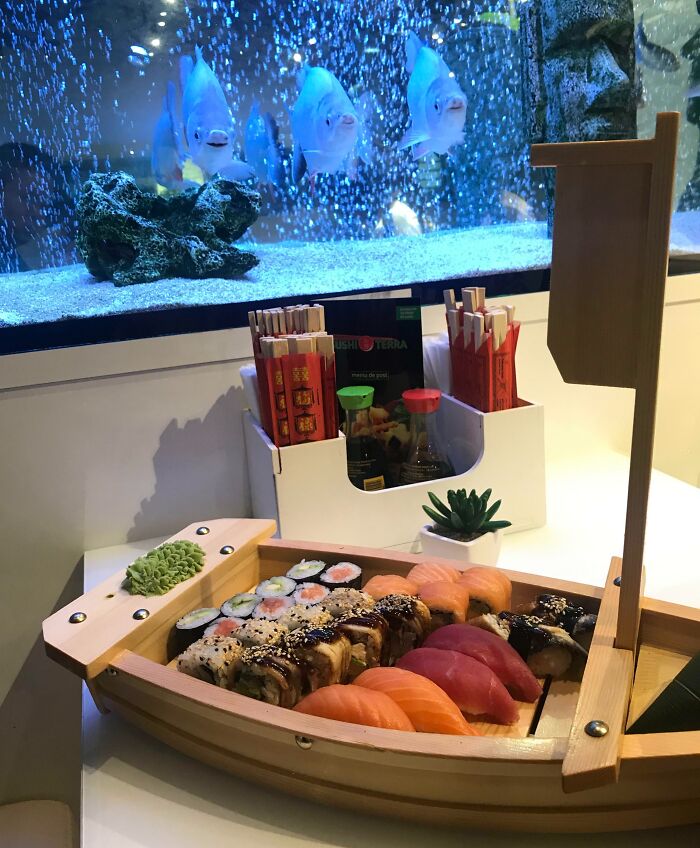 Creative sushi presentation on a wooden boat at a stylish bar and restaurant with an aquarium backdrop.