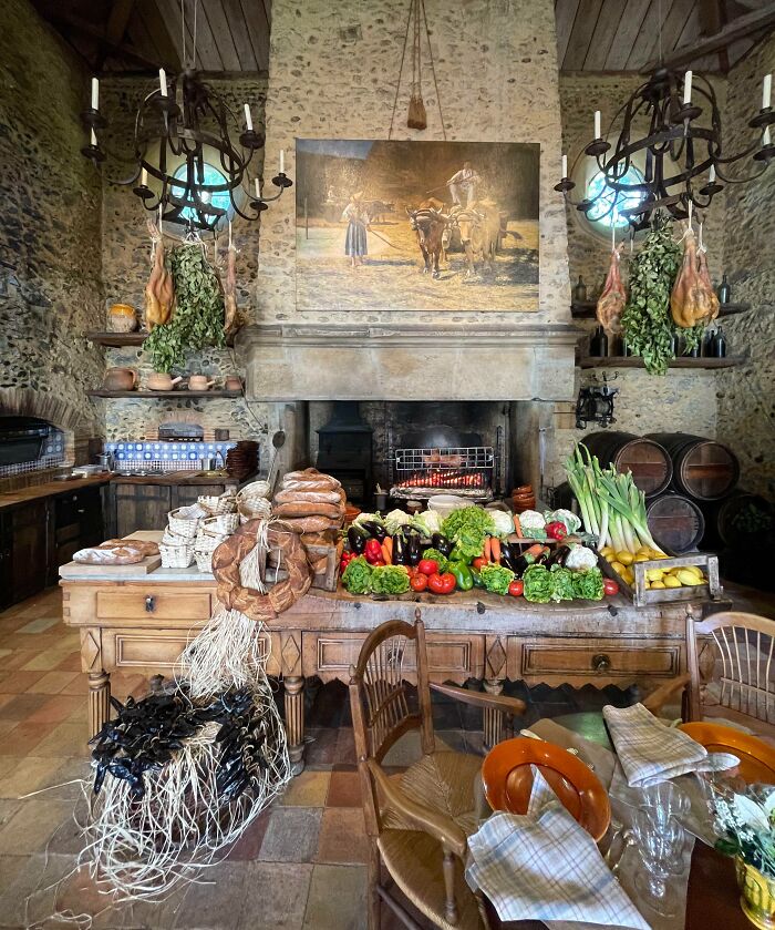 Rustic bar and restaurant interior with fresh produce, bread, hanging cured meats, and cozy stone walls showcasing creative decor.