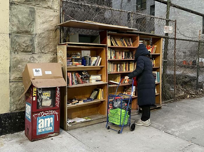 Person in a black coat browsing an outdoor free library, showcasing wholesome kind neighbors sharing books on the street. Person in a black coat browsing an outdoor free library, showcasing wholesome kind neighbors sharing books on the street.