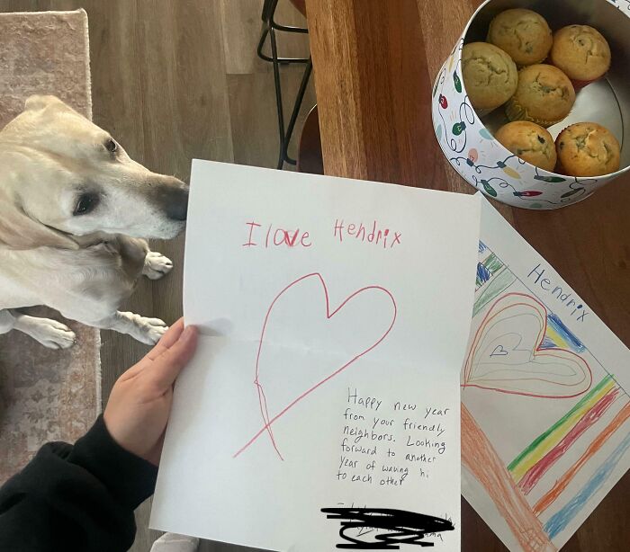 A person holding a handwritten note with a heart, a dog nearby, and muffins on a table, showing wholesome kind neighbors. A person holding a handwritten note with a heart, a dog nearby, and muffins on a table, showing wholesome kind neighbors.
