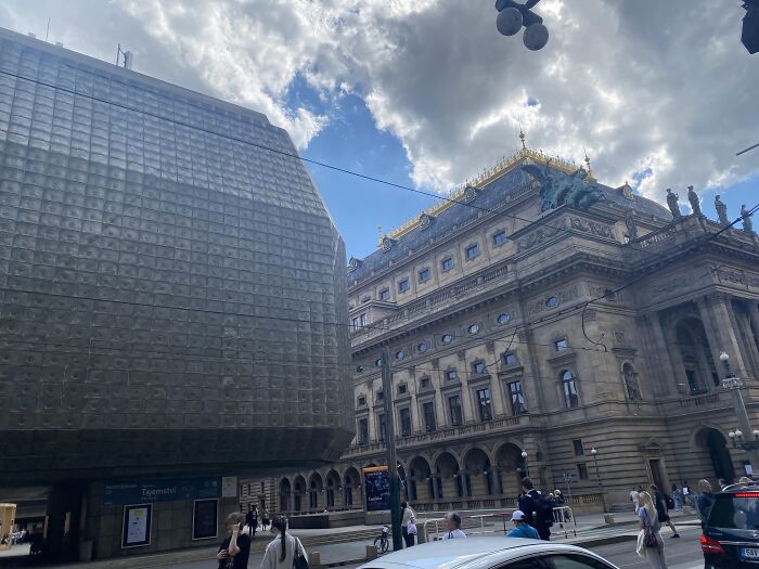 Contrasting old versus modern architecture with a historic ornate building next to a sleek modern glass structure under a cloudy sky.