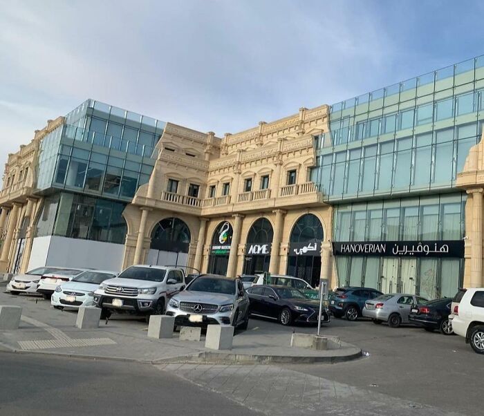 Blend of old versus modern architecture in a commercial building with classic stone facade and glass extensions under clear sky.