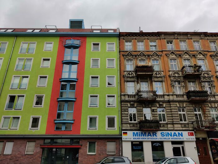 Old versus modern architecture showing a colorful modern building next to an ornate historic brick building under a gray sky.