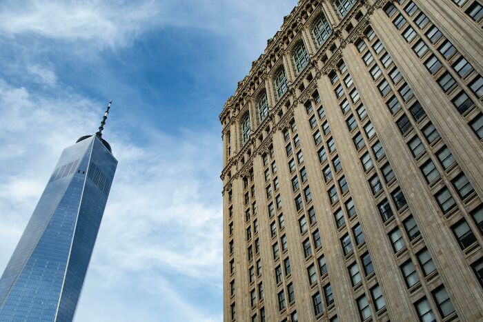 Old versus modern architecture shown with a historic stone building next to a sleek glass skyscraper under a blue sky.