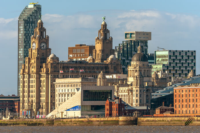 Old versus modern architecture showing historic clock towers and contemporary glass buildings along a waterfront cityscape.