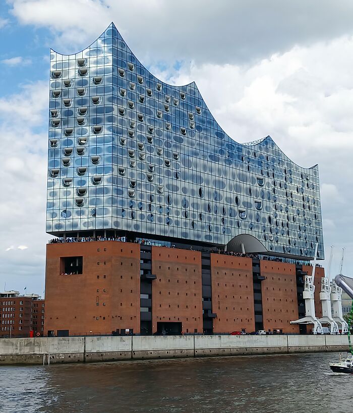 Modern architecture with a glass wave design atop a traditional brick building by the water showcasing old versus modern architecture.