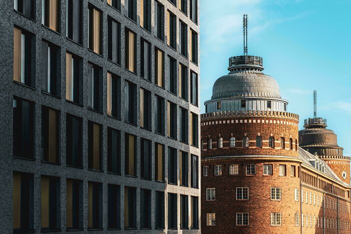 Modern building next to old brick architecture with round towers and detailed windows under a clear blue sky.